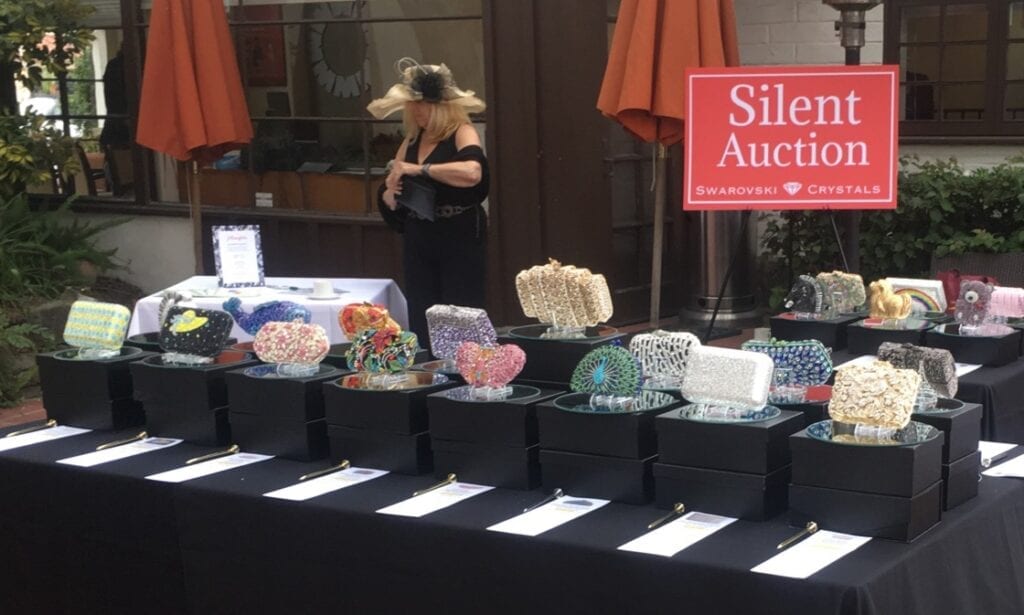 Various colorful handbags displayed on a table for silent auction.